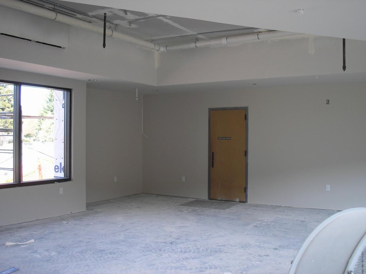 Wnętrze w trakcie prac wykończeniowych: szpachlowane ściany, sufit z widoczną instalacją, okno z folią ochronną.