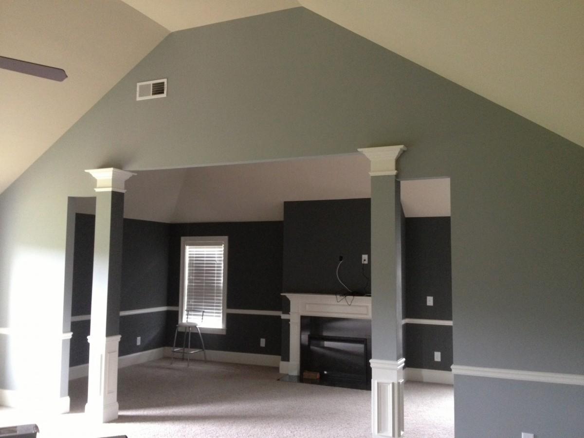 Pokój z kolumnami dekoracyjnymi, pomalowany na odcienie szarości, z kominkiem i wysokim sufitem ze skosami.