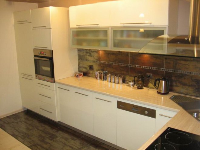 Jasna kuchnia z beżowym blatem, brązowymi płytkami imitującymi drewno na ścianie i nowoczesnymi sprzętami AGD.