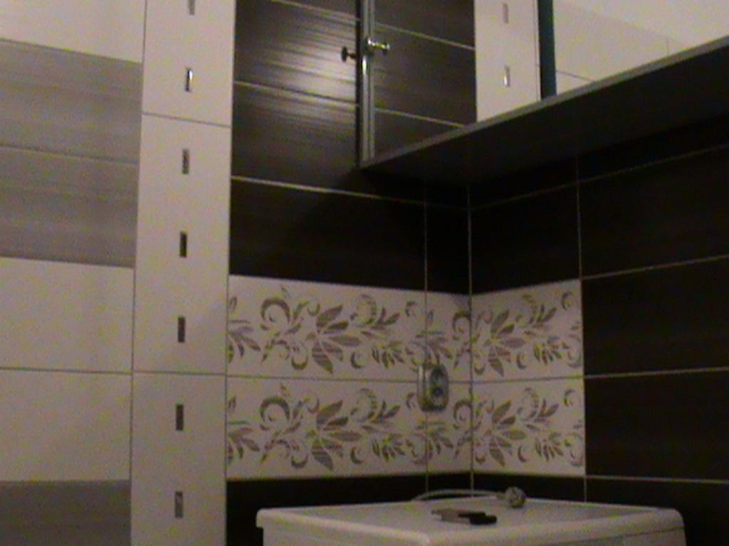 Wykończona łazienka z brązowo-białymi płytkami, dekoracyjnym motywem roślinnym na ścianie, białą szafką z lustrem i półką, widoczne akcesoria łazienkowe na umywalce.