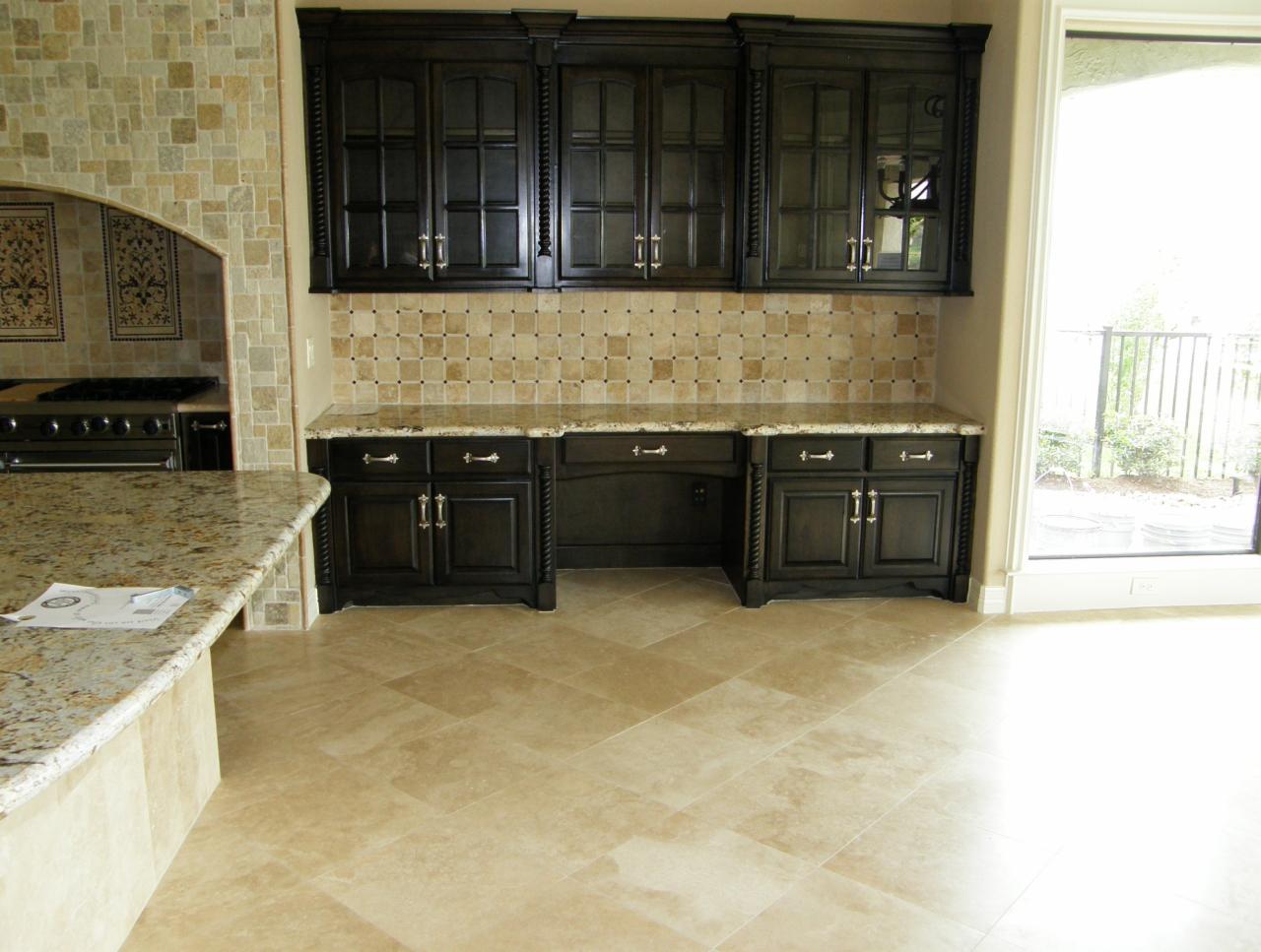 Wykończona kuchnia z ciemnymi szafkami, blatem z granitu i mozaikową ścianą nad blatem, widoczne płytki podłogowe i fragment wyspy kuchennej.