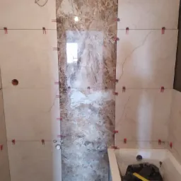 Układanie płytek w łazience w Parszowie, widoczne płytki imitujące marmur oraz system poziomowania płytek.