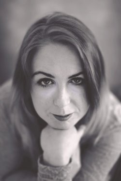 Portret kobiety w czerni i bieli, z dłonią pod brodą, skupionym spojrzeniem i delikatnym uśmiechem.