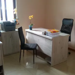 Jasne biuro z biurkiem, dwoma krzesłami, drukarką i żółtą orchideą w doniczce przy oknie.