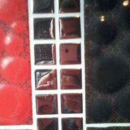 Wadowski Łukasz - Mozaika ścienna z czerwonymi, czarnymi i lustrzanymi kwadratami, ułożona w rzędach i kolumnach z białymi fugami, ukazująca odbicie dłoni w jednym z lustrzanych elementów.