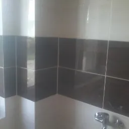 Fragment wykończonej ściany łazienki z dwukolorowymi, błyszczącymi płytkami ceramicznymi (białe i imitujące ciemne drewno) oraz widocznym fragmentem baterii umywalkowej.