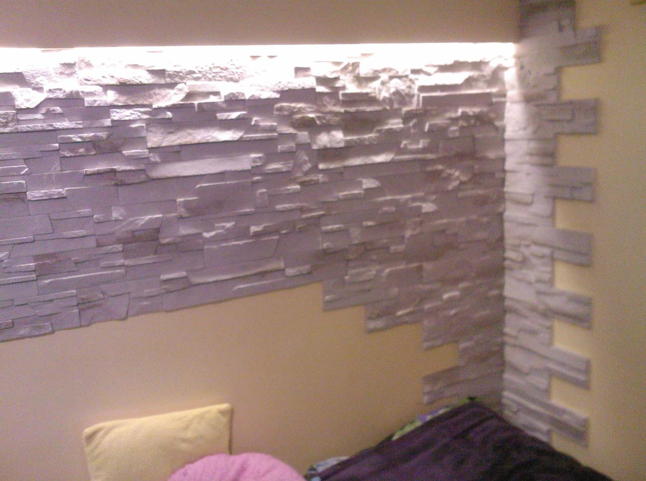 Ściana wykończona dekoracyjną okładziną z szarego kamienia imitującego łupek, z podświetleniem LED u góry, częściowo przylegająca do pomalowanej ściany w odcieniu ciepłego beżu, widoczny narożnik...