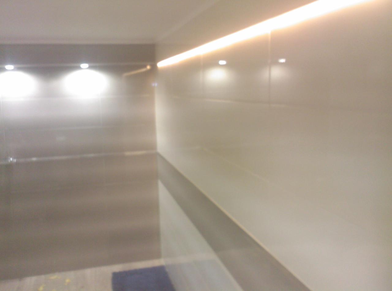 Wykończona łazienka z białymi płytkami, podświetleniem LED podsufitowym i szarą listwą przypodłogową oraz fragmentem niebieskiego dywanika w rogu.