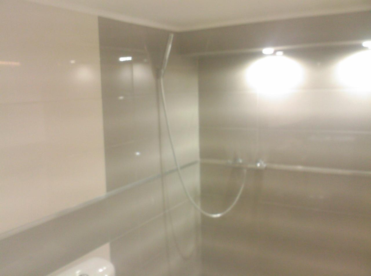 Nowoczesna kabina prysznicowa z deszczownicą, wykończona jasnymi płytkami ceramicznymi i oświetleniem punktowym.