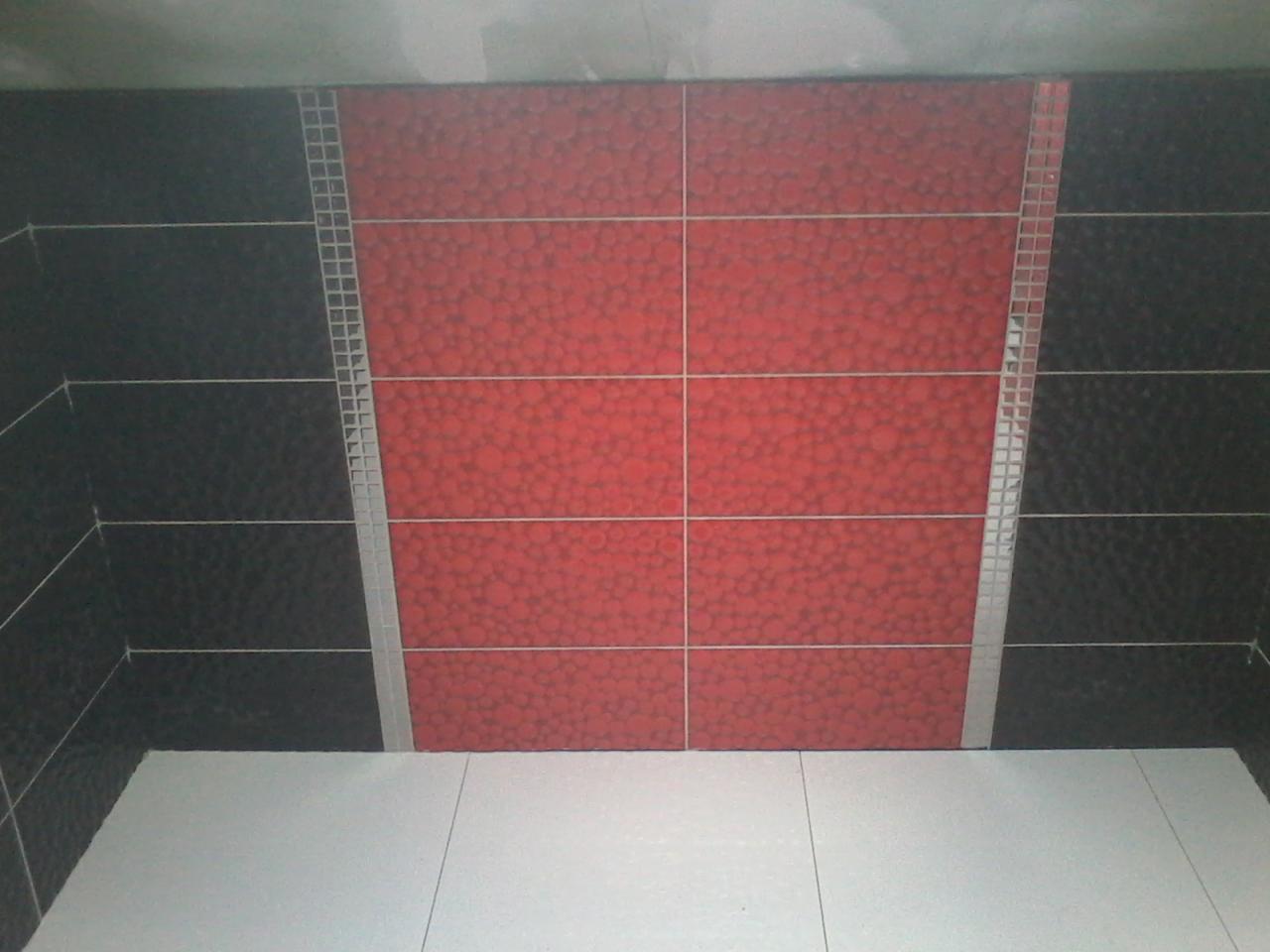 Fragment ściany łazienki z czarnymi i czerwonymi płytkami z dekoracyjną listwą mozaikową, biała podłoga z płytek.