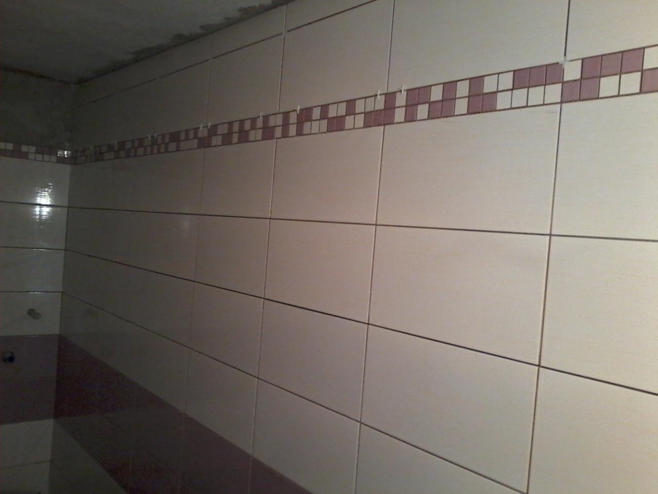 Ściana wyłożona białymi, poziomymi płytkami z dekoracyjnym pasem z fioletowo-białej mozaiki, widoczne krzyżyki dystansowe w spoinach.