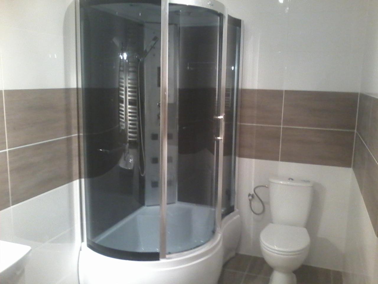 Kabina prysznicowa z hydromasażem, widoczna w rogu łazienki z brązowo-białymi płytkami i toaletą.