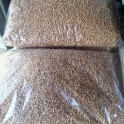 Dwa duże, przezroczyste worki wypełnione pelletem drzewnym, ułożone jeden na drugim na drewnianej palecie.