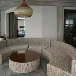 Zadaszone patio z narożną sofą z rattanu, okrągłym stolikiem kawowym z brązowym blatem i kamiennym kominkiem w tle.