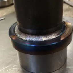 Metalowa rura połączona precyzyjnym spoiwem spawalniczym, widoczne tęczowe przebarwienia termiczne na obrzeżach spoiny.