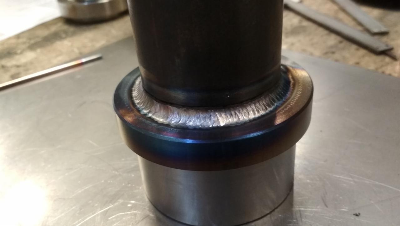 Metalowa rura połączona precyzyjnym spoiwem spawalniczym, widoczne tęczowe przebarwienia termiczne na obrzeżach spoiny.