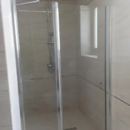 Nowoczesna kabina prysznicowa z przesuwnymi drzwiami, wykończona płytkami w odcieniach beżu i szarości, z widocznym odpływem liniowym w podłodze.