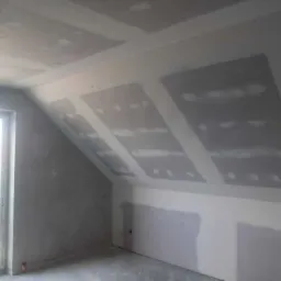 Poddasze w Mikstacie w trakcie montażu płyt karton-gips na skośnym suficie, widoczne łączenia płyt wymagające szpachlowania, surowe wykończenie.