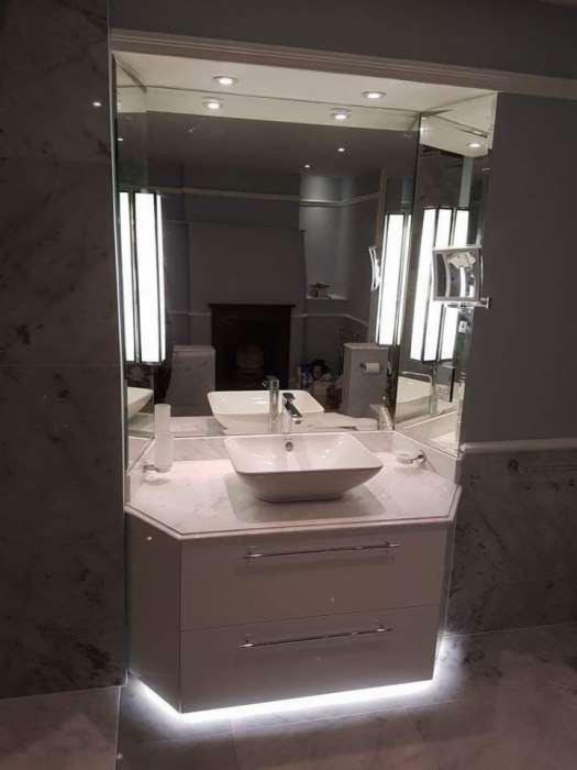 Nowoczesna łazienka z podświetlaną szafką pod umywalką, lustro z oświetleniem po bokach, marmurowe ściany i podłoga.