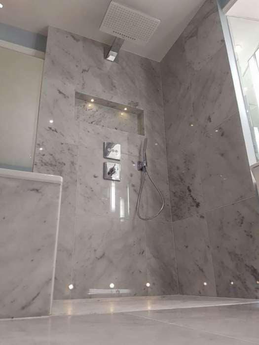 Wykończona łazienka z kabiną prysznicową wyłożoną marmurowymi płytami, podświetlonymi punktowo oraz w niszy ściennej.