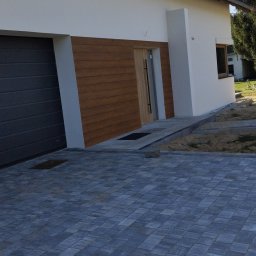 MiKO COMPLEX MICHAŁ KOZŁOWSKI - Nowoczesny dom jednorodzinny z elewacją w kolorze bieli i drewna, szara kostka brukowa na podjeździe, widok z boku.