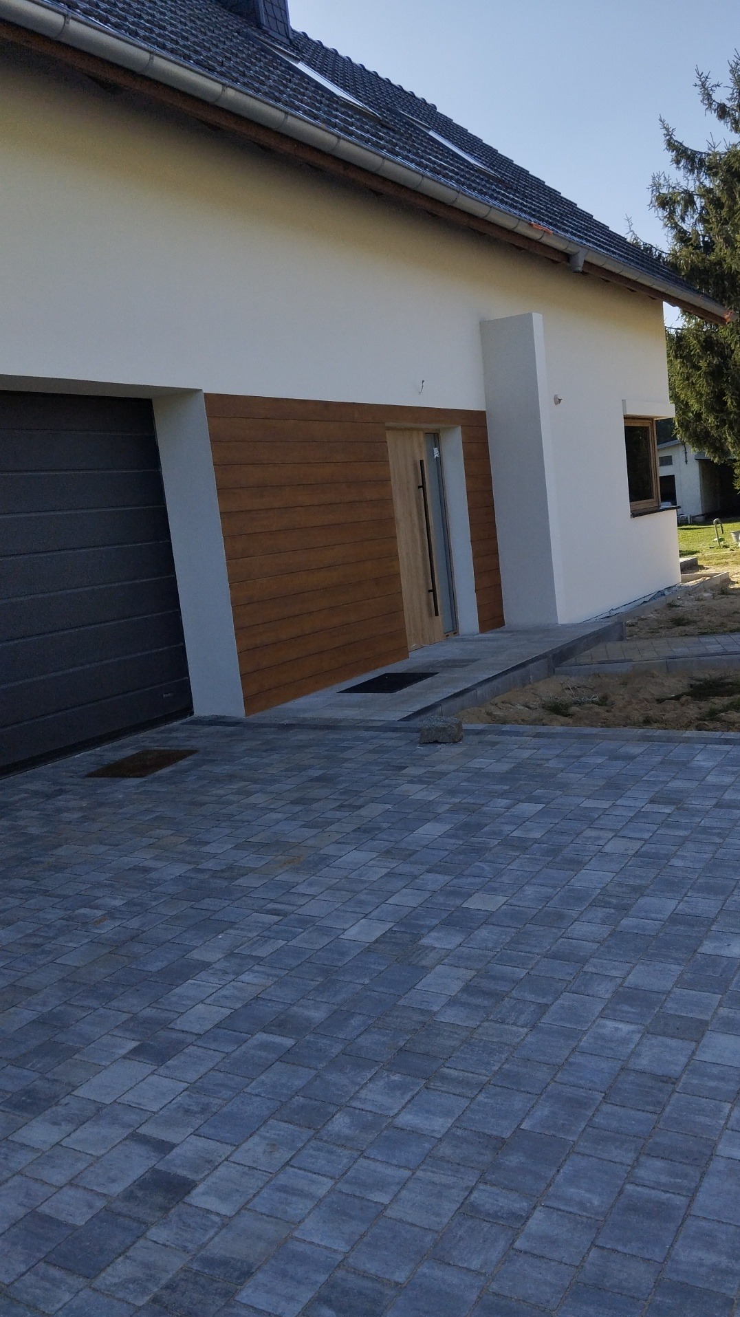 Nowoczesny dom jednorodzinny z elewacją w kolorze bieli i drewna, szara kostka brukowa na podjeździe, widok z boku.