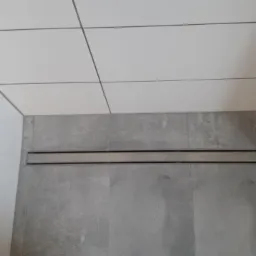 Nowoczesna kabina prysznicowa z odpływem liniowym, wykończona białymi i szarymi płytkami ceramicznymi.