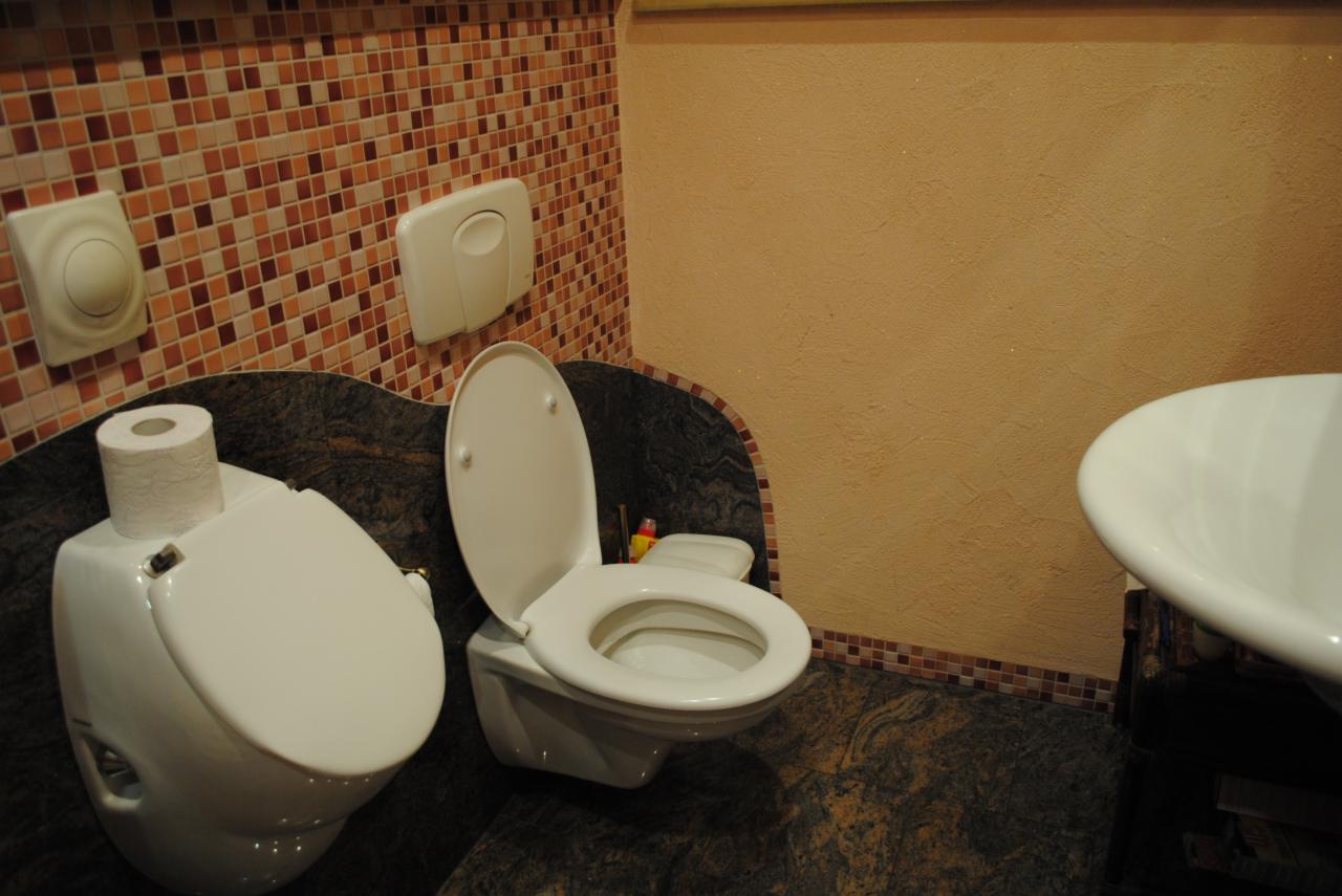 Wykończona łazienka z dwoma toaletami w stylu retro, brązowe mozaiki na ścianach i podłodze z ciemnego granitu.