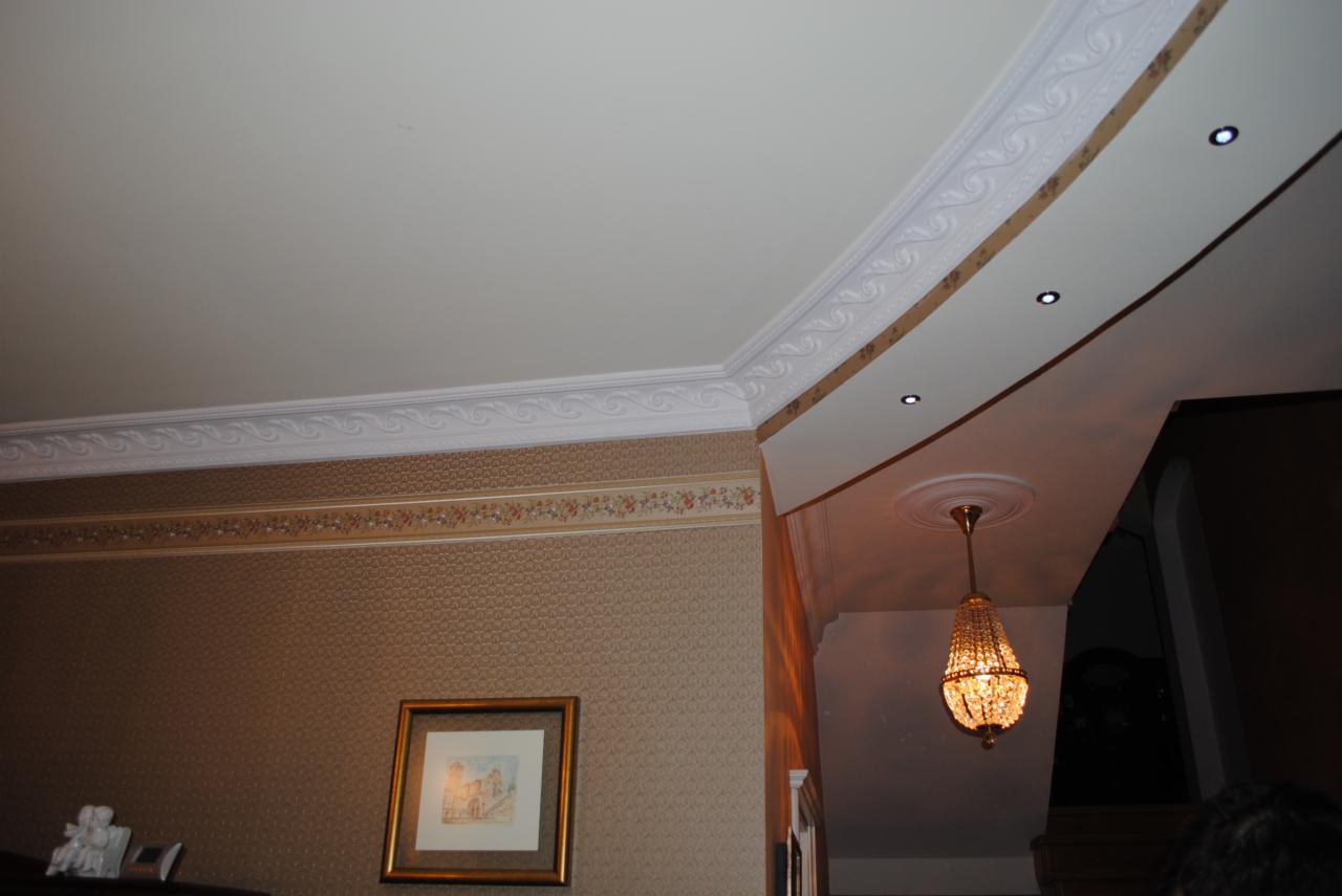 Wnętrze z dekoracyjnymi listwami przysufitowymi, wzorzystą tapetą, oświetleniem punktowym i kryształowym żyrandolem.