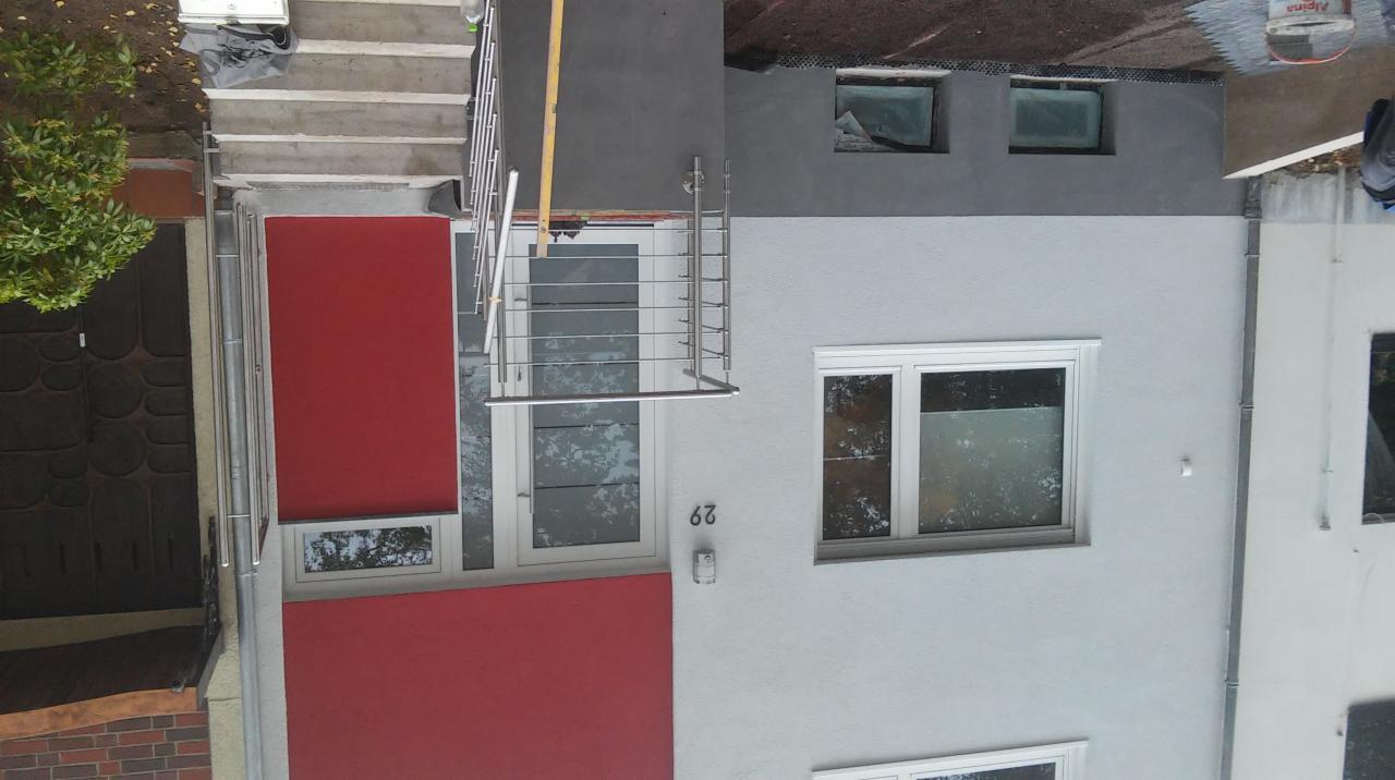 Dwukondygnacyjny budynek z czerwonymi i szarymi elementami elewacji po remoncie, widok z góry, z numerem 62 na ścianie.