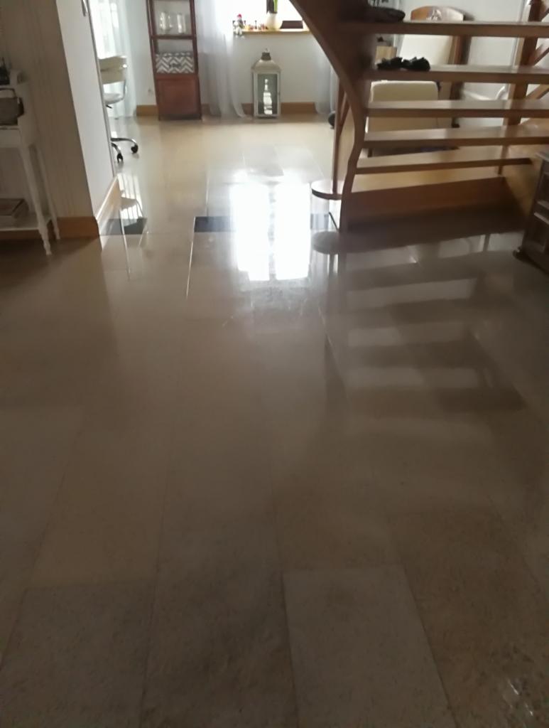 Błyszcząca, beżowa podłoga z płytek w przestronnym wnętrzu, widoczne schody drewniane i fragmenty mebli w tle