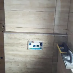 Ściana łazienki wyłożona płytkami imitującymi drewno, z widoczną instalacją podtynkową WC i narzędziem do fugowania płytek.