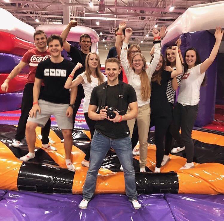 Grupa młodych ludzi, w tym fotograf z aparatem na szyi, świętuje na dmuchanym placu zabaw, unosząc ręce w geście radości.