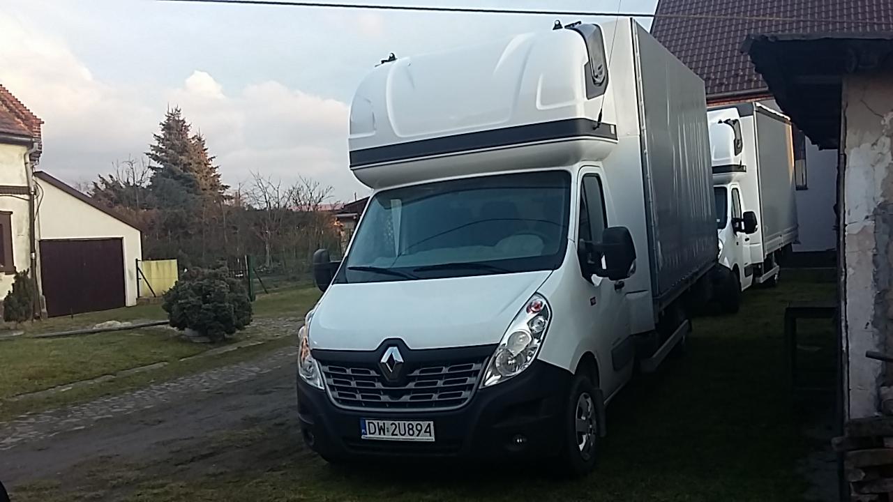 Biały Renault Master z wysoką zabudową skrzyniową zaparkowany na trawniku, widoczne tablice rejestracyjne DW 2U894, w tle kolejne busy i zabudowania gospodarcze.
