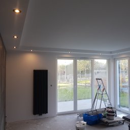 mario-dario - Wnętrze w trakcie remontu w Gdańsku: zamontowane grzejniki panelowe, sufit podwieszany z oświetleniem punktowym i widoczne narzędzia malarskie przy oknach.