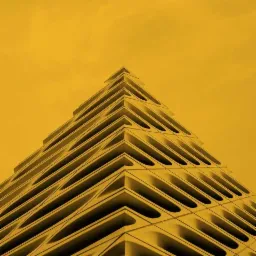 Żółta, abstrakcyjna fasada budynku z powtarzalnymi, geometrycznymi elementami przypominającymi piramidę schodkową.