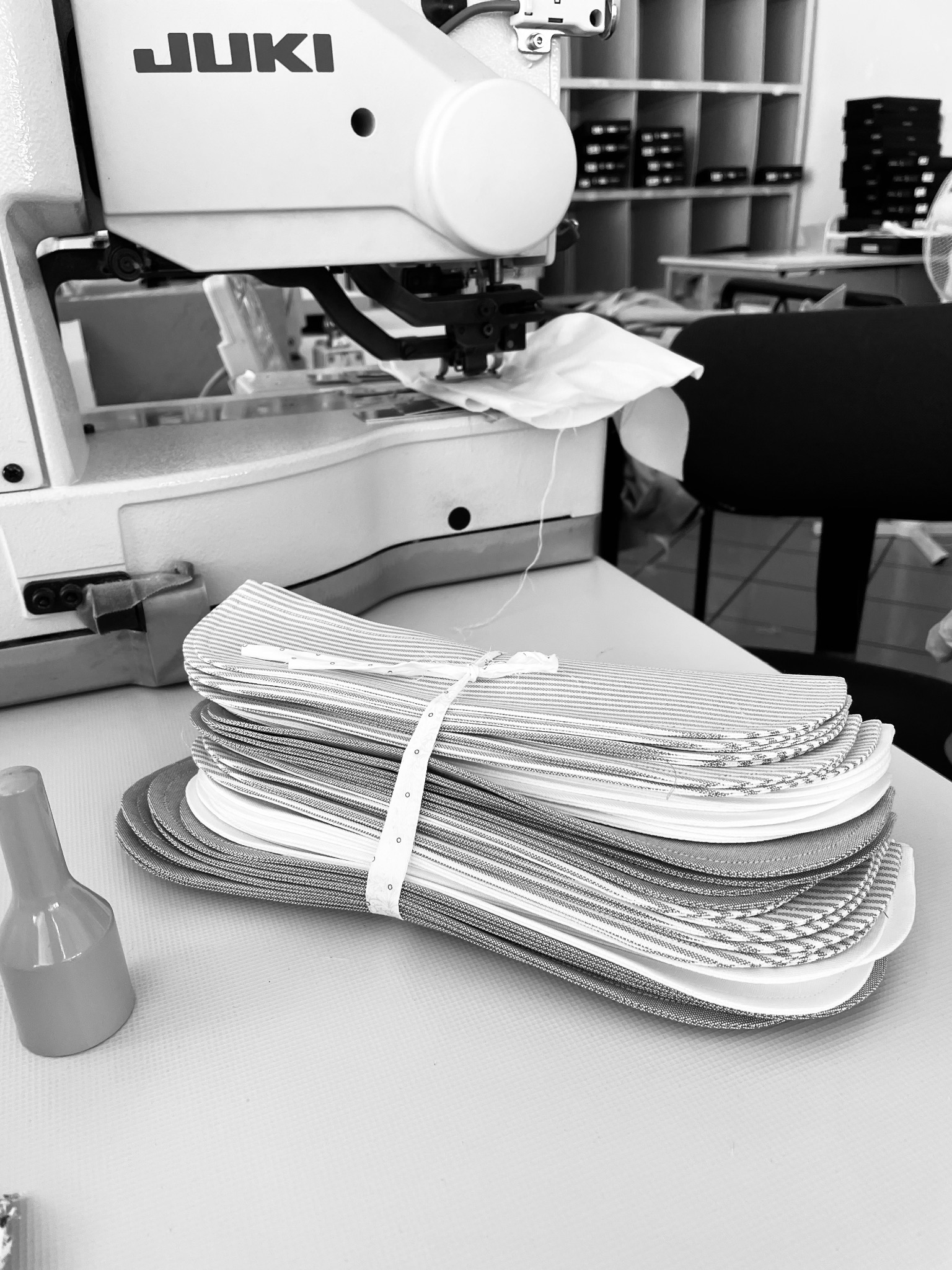 Stos pociętych elementów odzieży, związanych tasiemką, leżący na stole obok maszyny do szycia JUKI w szwalni.