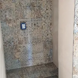 Wykończona kabina prysznicowa w Mucharzu z dekoracyjnymi płytkami ceramicznymi na ścianach i podłodze, widoczny odpływ liniowy i fragment instalacji wodnej.