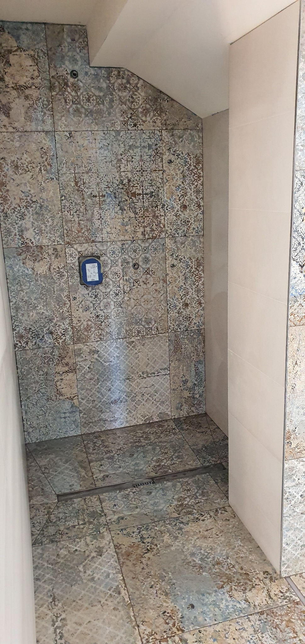 Wykończona kabina prysznicowa w Mucharzu z dekoracyjnymi płytkami ceramicznymi na ścianach i podłodze, widoczny odpływ liniowy i fragment instalacji wodnej.