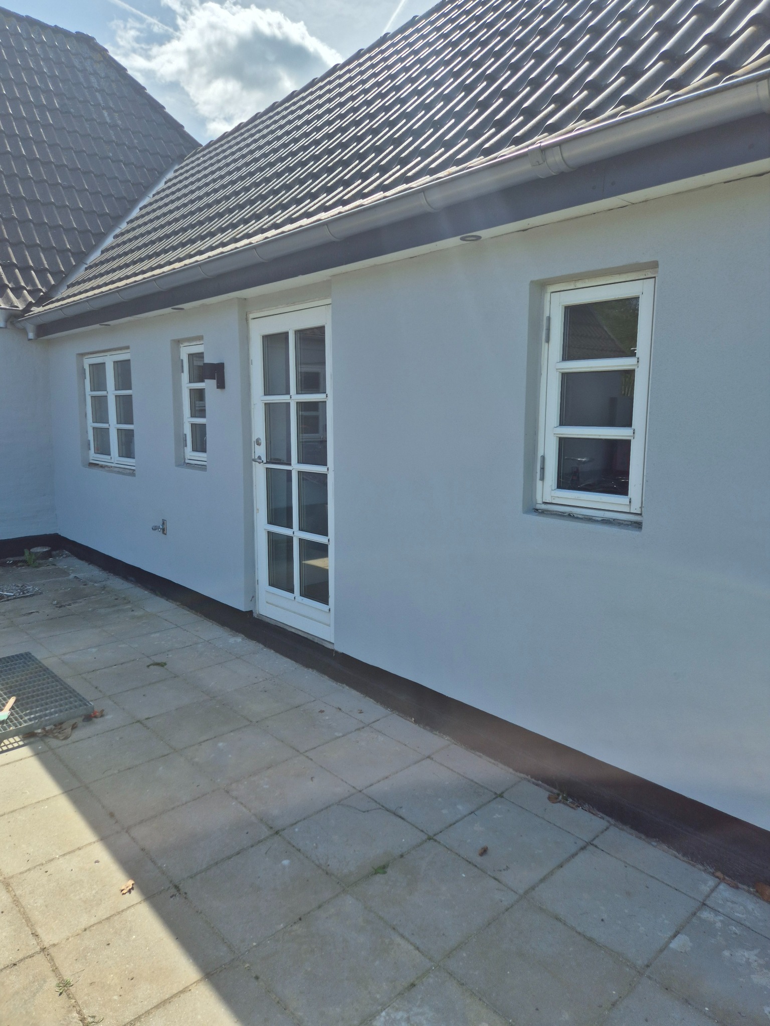 Odnowiona elewacja domu w Otterup z białymi oknami i drzwiami, świeżo po pracach wykończeniowych. Jasnoszary kolor ścian, widok z zewnątrz na taras.