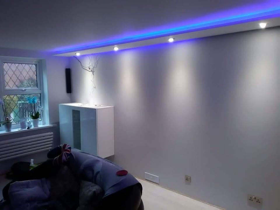 Pokój z szarą ścianą, oświetleniem LED w kolorze niebieskim, białym regałem, grzejnikiem pod oknem i dekoracją ścienną w kształcie drzewa.