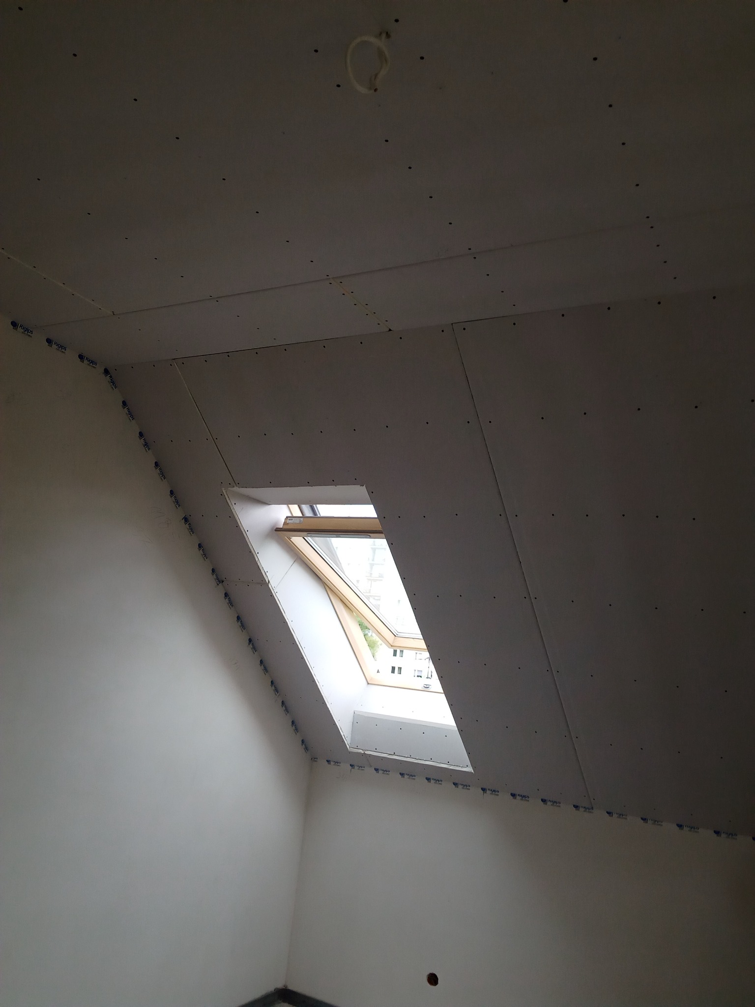 Montaż płyt karton-gips na poddaszu w Gilowicach, widoczne okno dachowe i przytwierdzone płyty, przygotowane do dalszej obróbki.
