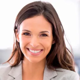 Portret uśmiechniętej brunetki w szarym żakiecie, z widocznymi dołeczkami w policzkach i jasnym tłem, sugerujący profesjonalizm i zaufanie.