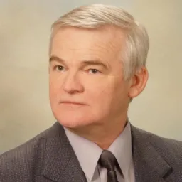 Portret mężczyzny w szarym garniturze i krawacie, z siwymi włosami, na neutralnym tle.