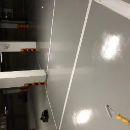 Szara posadzka żywiczna w garażu podziemnym z wyznaczonymi białymi liniami, widoczny wałek malarski z żółtą rączką.