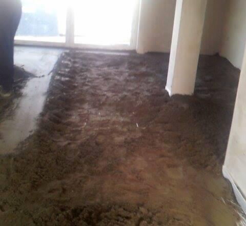 Świeżo wylana, jeszcze mokra, brązowa masa na podłodze w pomieszczeniu z kolumnami, widoczne ślady po narzędziach.