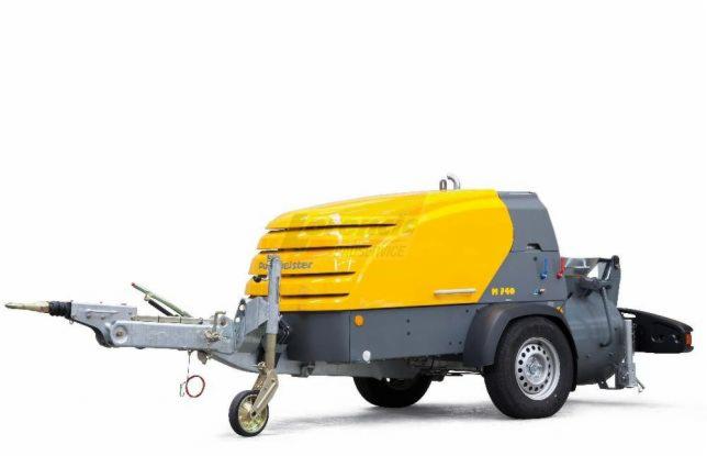 Żółto-szara pompa do wylewek Putzmeister M 740 na przyczepie, widok z boku na białym tle.