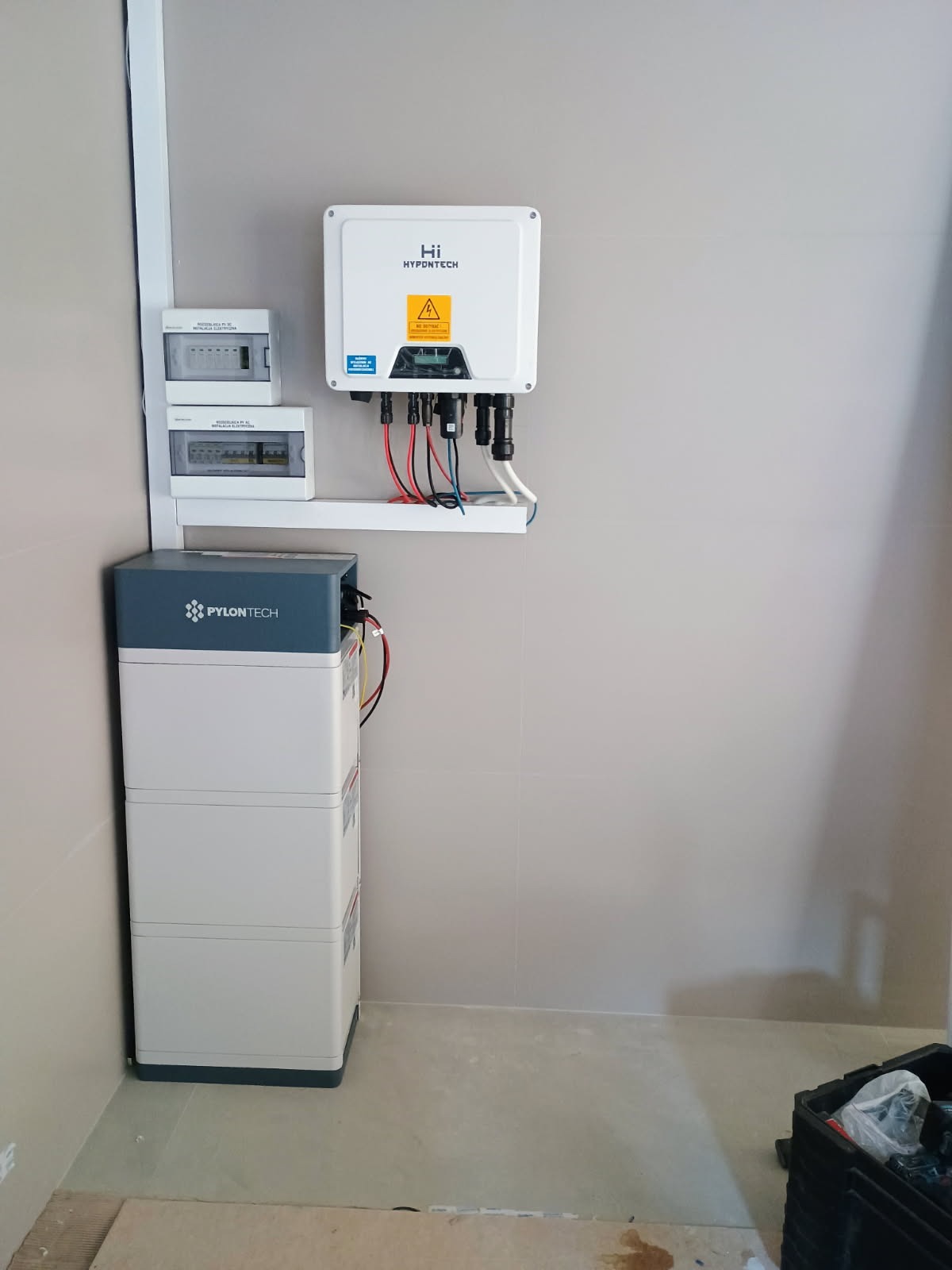 Zestaw akumulatorów Pylontech i inwerter Hypontech zamontowane na ścianie w pomieszczeniu, z widocznymi przewodami i skrzynkami elektrycznymi.