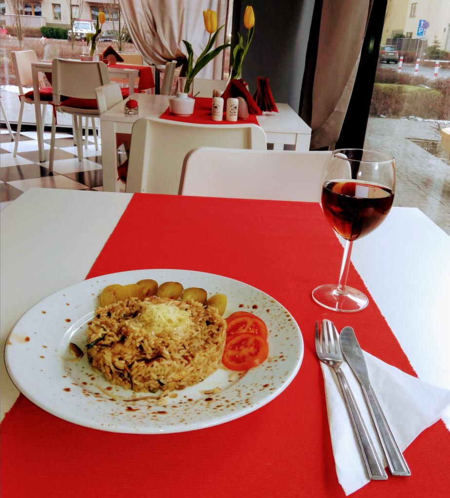 Elegancko podane danie z ryżu z warzywami i serem, pieczone ziemniaki, plastry pomidora oraz kieliszek czerwonego wina na stole z czerwonym obrusem w restauracji.