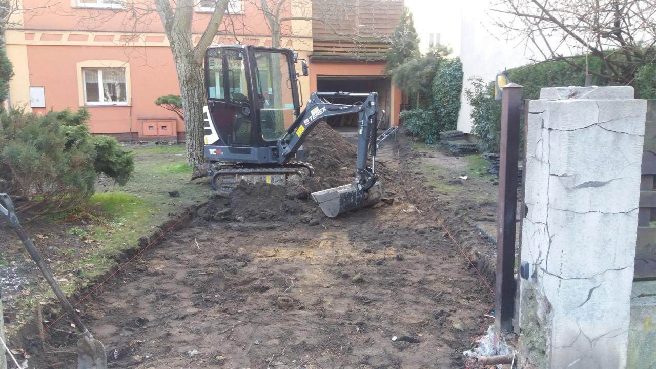 Minikoparka Terex TC na posesji podczas przygotowywania terenu pod przyszły podjazd, widoczne wytyczone krawędzie oraz stara brama wjazdowa z popękanymi słupkami.